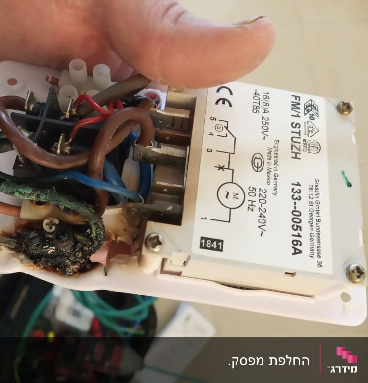 חוטי חשמל שרופים וממסר חשמלי ביד חשמלאי